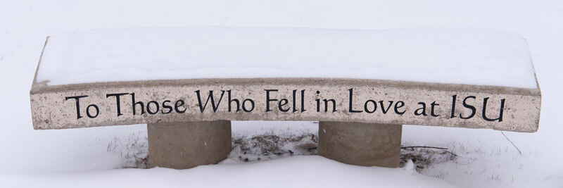 A stone bench in the snow that reads 'To Those Who Fell in Love at ISU'.