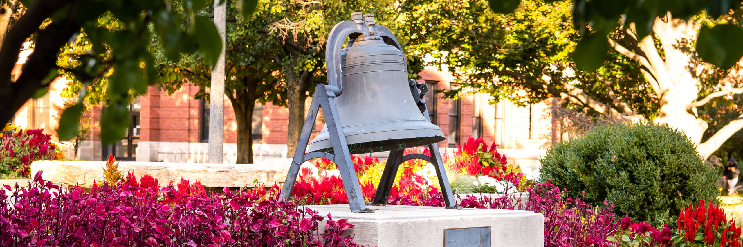 Old Main Bell surrounded by flowers.