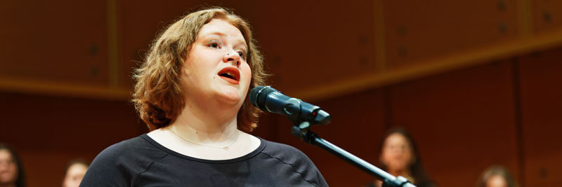 A student sings into a microphone during a choral performance.