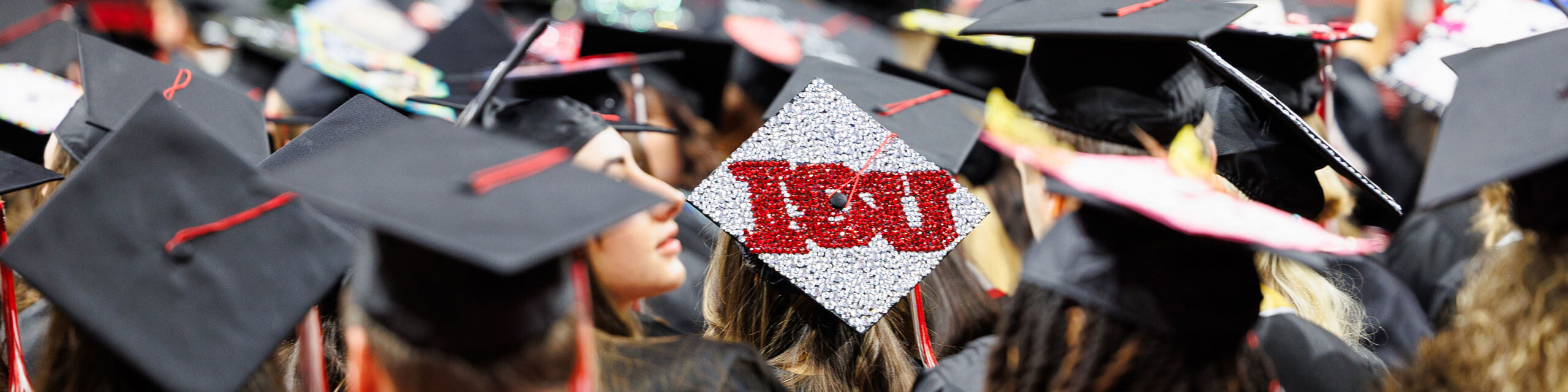 A graduate in a crowd of their peers wears a cap that reads 'ISU'.